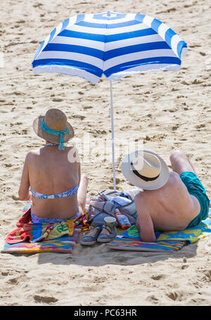 Bournemouth, Dorset, Großbritannien. 31. Juli 2018. UK Wetter: Die Sonne kommt wieder und die Temperaturen steigen, wie Strand - goers Kopf an der Küste des warmen und sonnigen Wetter zu genießen. Reifes Paar Sonnenbaden am Strand mit Sonnenschirm. Credit: Carolyn Jenkins/Alamy leben Nachrichten Stockfoto