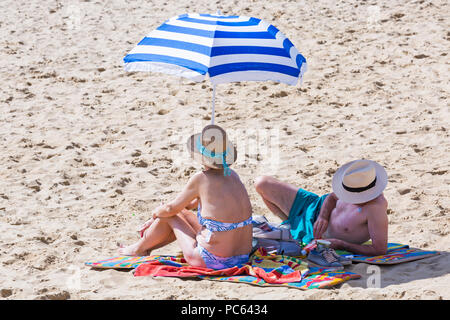 Bournemouth, Dorset, Großbritannien. 31. Juli 2018. UK Wetter: Die Sonne kommt wieder und die Temperaturen steigen, wie Strand - goers Kopf an der Küste des warmen und sonnigen Wetter zu genießen. Reifes Paar Sonnenbaden am Strand mit Sonnenschirm. Credit: Carolyn Jenkins/Alamy leben Nachrichten Stockfoto