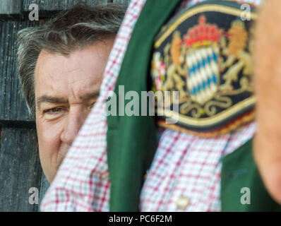 Hausham, Deutschland. 01 Aug, 2018. Markus Soeder (L) der Christlich Sozialen Union (CSU), Ministerpräsident von Bayern, sitzt in der Kreuzbergalm Biergarten hinter dem bayerischen Wappen, die auf das Kostüm eines Teilnehmers in der alpinen Wanderung abgenutzt ist. Wegen der anhaltenden Hitze, in diesem Jahr weniger Menschen nahmen an der jährlichen wichtigsten Alm Inspektion der Alm Management Association. Credit: Lino Mirgeler/dpa/Alamy leben Nachrichten Stockfoto