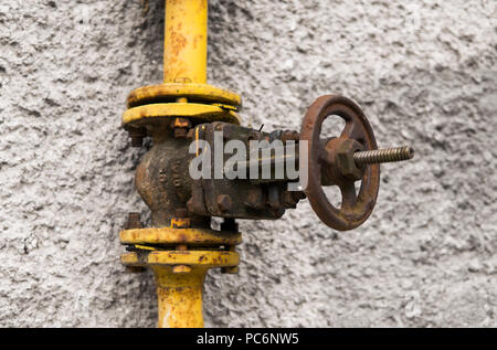 Alte verwitterte gas Kran und Rohr auf dem Hintergrund einer graue Wand. Alte gas- tor der gelbe Farbe ist auf einer Rohrleitung und Bausteine einer Rohrleitung. Die Pipeline mit Kränen für Gas geben auf der Wand. Stockfoto