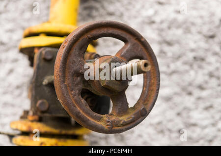 Alte verwitterte gas Kran und Rohr auf dem Hintergrund einer graue Wand. Alte gas- tor der gelbe Farbe ist auf einer Rohrleitung und Bausteine einer Rohrleitung. Die Pipeline mit Kränen für Gas geben auf der Wand. Stockfoto