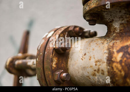 Alte verwitterte gas Kran und Rohr auf dem Hintergrund einer graue Wand. Alte gas- tor der gelbe Farbe ist auf einer Rohrleitung und Bausteine einer Rohrleitung. Die Pipeline mit Kränen für Gas geben auf der Wand. Stockfoto