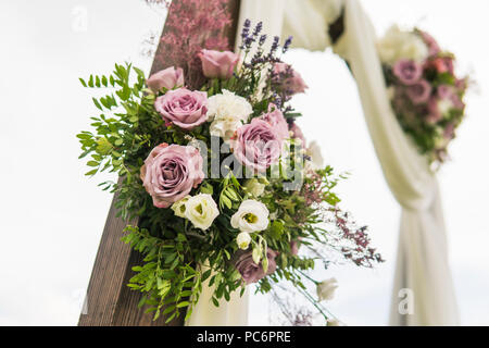 Blumen Holz- Bogen mit einem weißen Tuch und frisches violett rosa-weißen Blüten mit grünen Blättern auf eine rustikale Hochzeit. Stockfoto