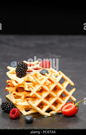 Foto von Wiener Wafer mit Beeren gießen Honig auf schwarzem Hintergrund Stockfoto