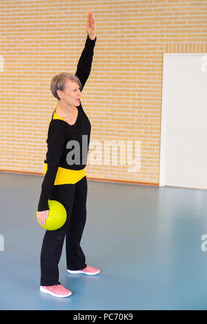 Sportlehrer mit Kugel erstreckt sich Armmuskeln als Übung in der Turnhalle Klasse Stockfoto