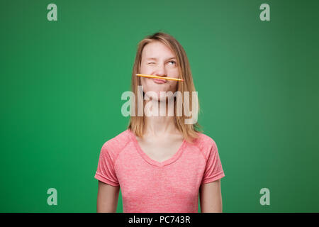 Lustige Student in Rosa t-shirt spielen die Feder zwischen Nase und Lippen, als Schnurrbart. Stockfoto