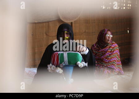 Eine Frau mit einem metallischen Burka strickt Emiratische Flag im Heritage Village in Fujairah. Das Dorf ist zu Reihen, die Emiratische Kultur. Stockfoto