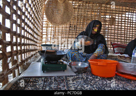 Eine Frau, sporting ein metallisches Burka, Köche Süßigkeiten zu ihrer Hütte im Heritage Village in den Vereinigten Arabischen Emiraten Fujairah. Stockfoto