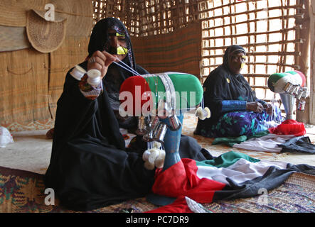 Eine Frau mit einem metallischen Burka strickt Emiratische Flag im Heritage Village in Fujairah. Das Dorf ist zu Reihen, die Emiratische Kultur. Stockfoto