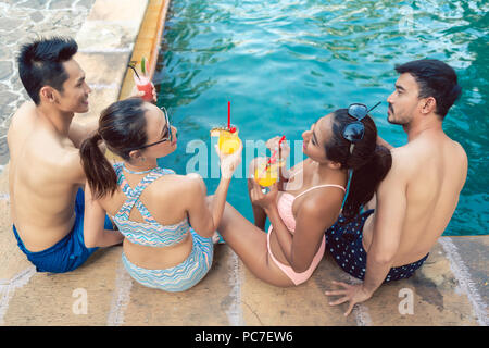 Zwei junge Paare trinken Cocktails während der Entspannung am Pool Stockfoto