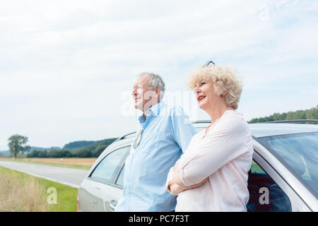 Zwei ältere Menschen lächelnd mit Vertrauen und lehnte sich auf Ihr Auto Stockfoto
