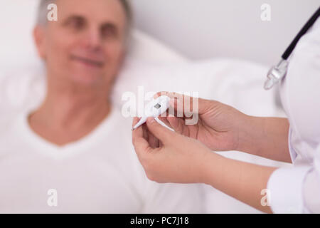 Nahaufnahme therometer Krankenschwestern in Händen. Weibliche Hände von Arzt holding Thermometer. Ältere Patienten unscharf im Hintergrund. Stockfoto