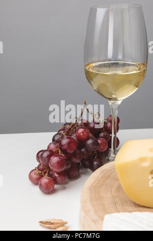 Teilweise mit Blick auf die maasdamer Käse auf Holzbrett, Glas Wein, Mandeln und Trauben auf Grau Stockfoto