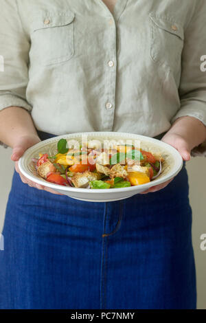 Eine Frau hält ein Schild mit einem panzanella Salat in den Händen. Im rustikalen Stil. Stockfoto