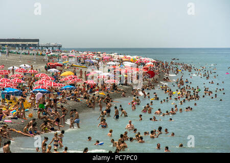 Horden von Sonnenanbetern und Strandurlauber Masse der Kies und schwarzem Sand und schwimmen im Schwarzen Meer von Batumi, Georgien. Stockfoto