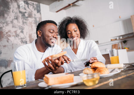 Lächelndes Paar Verbreitung Stau auf Toast am Tisch mit Frühstück Stockfoto