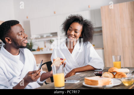 Lächelnde Menschen verbreiten Stau auf Toast und Freundin sitzen am Tisch mit Frühstück Stockfoto