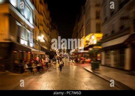 Verschwommene Bewegung Bild von Menschen zu Fuß auf der Straße vorbei an Cafés und Bistros in der Nacht in Paris. Stockfoto