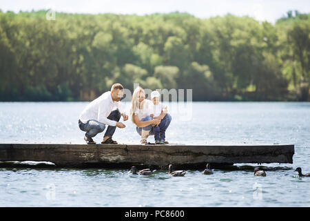 Glückliche Mutter, Vater und Sohn, füttern Sie die Enten an einem sonnigen Tag Stockfoto