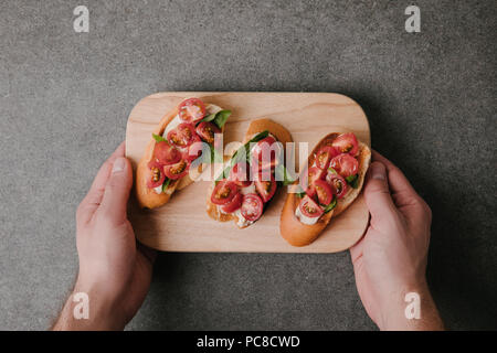 7/8 Schuß von Person holding Holzbrett mit köstlichen Tomaten Bruschetta Stockfoto