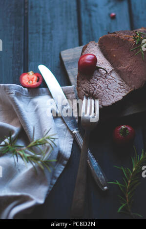 Gebackenes Fleisch mit Rosmarin und rotem Pfeffer. Steak. Rindfleisch. Abendessen für Männer. Dunkle Foto. Schwarzen Hintergrund. Holzbrett Stockfoto