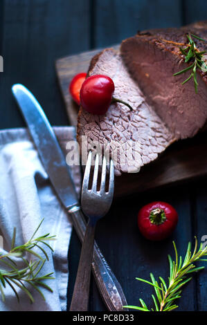 Gebackenes Fleisch mit Rosmarin und rotem Pfeffer. Steak. Rindfleisch. Abendessen für Männer. Dunkle Foto. Schwarzen Hintergrund. Holzbrett Stockfoto