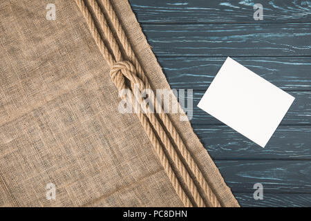 Blick von oben auf die nautischen Seil geknotet Braun am Sack und leeres Papier auf Holz- Oberfläche Stockfoto