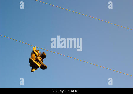 Alte Turnschuhe hängen auf Dienstprogramm power line mit klaren blauen Himmel. Stockfoto