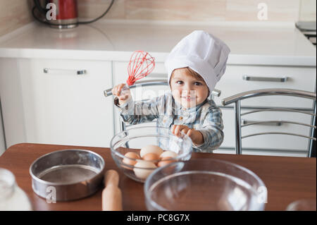 Adorable kleine Zicklein in der Küchenchef hat mit Schneebesen und Eier Stockfoto