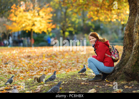 Junge weibliche Touristen füttern Eichhörnchen und Tauben in St. James Park in London, Vereinigtes Königreich, auf schönen sonnigen Tag im November. Stockfoto