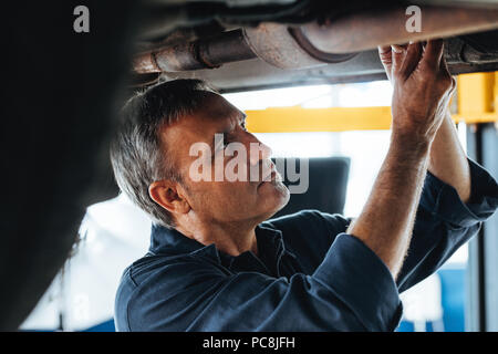 Porträt von einem Mechaniker bei der Arbeit in seiner Garage. Reifen auto Techniker arbeiten unter einem Auto Service Station. Stockfoto