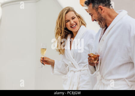 Freundliche Paar in Bademantel Sprechen und Lachen. Der Mann und die Frau in der Bademäntel mit einem Glas Wein und lächelnd. Stockfoto