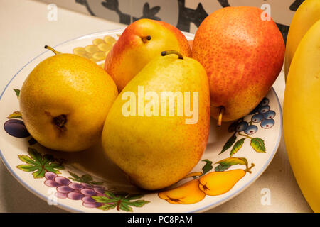 Vier Bartlett Birnen, Pyrus Communis, in einen Teller mit Obst dekoriert. Nahaufnahme. Stockfoto