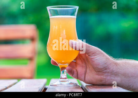 Männliche Hand ein Glas kaltes Bier auf einem Tisch im Garten Stockfoto