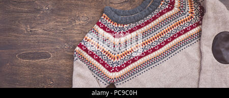 Grau, Orange, Bordo und beige gestrickter Pullover auf hölzernen Hintergrund Stockfoto