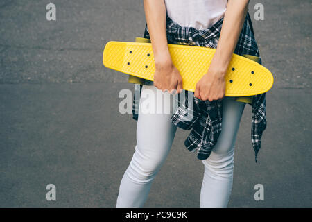 Close-up junge Frau mit Kunststoff Skateboard. Teenage student Mädchen in Jeans und Shirt bis auf den Hüften stehen mit ihren gelben Penny board gebunden auf Stockfoto