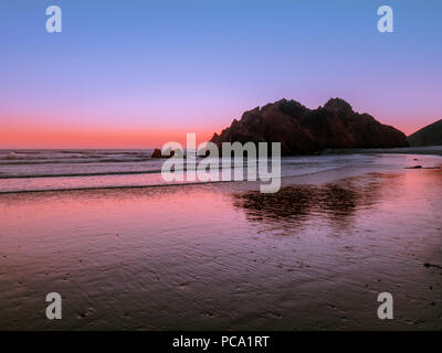 Felsige Klippe Reflexionen auf dem nassen Sand von Pfeiffer Big Sur Beach in Kalifornien in der blauen Stunde nach Sonnenuntergang. Low Angle Shot mit klaren Himmel Gradienten. Stockfoto