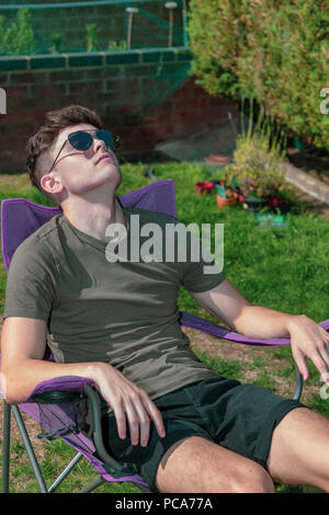 Junge Erwachsene draußen zu sitzen und genießen Sie die Sommersonne in einem Garten Stockfoto
