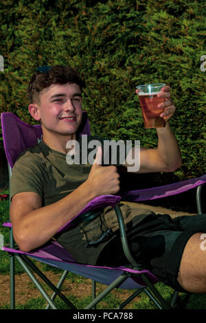 Junge Erwachsene außerhalb genießen den Sommer Sonnenschein mit einem Bier in einem Garten Stockfoto