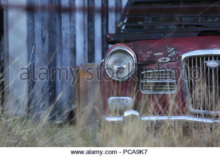 Ein altes rostiges Auto hebt ungenutzte wie Gras wächst es in der Nähe von einem verfallenen Haus. Stockfoto