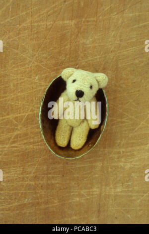 Kleine beige Teddybär liegend in der einen Hälfte der eiförmige Messing Pillenschachtel auf zerkratzte Holz Stockfoto