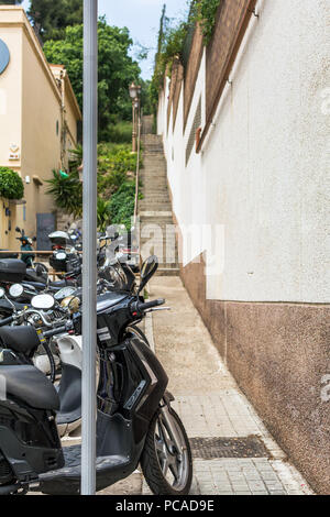 Bündel von Motorrollern in sehr schmalen Straße mit Treppen in Barcelona geparkt. Stockfoto