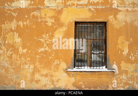 Einen vergitterten Fenster auf die alte gelbe Wand mit einem schneebedeckten Fensterbank. Stockfoto