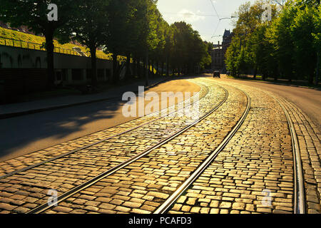 Lettland, Riga. Abends Sonnenlicht auf einer Biegung der Straße mit Straßenbahnschienen Kopfsteinpflaster in der Nähe des Parks Stockfoto