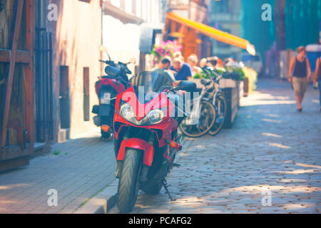 Lettland. Riga. 2015. Sommer. Rotes Motorrad im Sommer Cafe mit einem gelben Markise und flanieren Touristen an einem sonnigen Tag Stockfoto