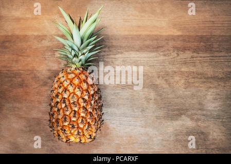 Single eine volle ganze Bio Ananas Obst auf hölzernen Hintergrund reifen Erwachsenen Reife, unten auf der Seite negative leeren Raum für Text Stockfoto