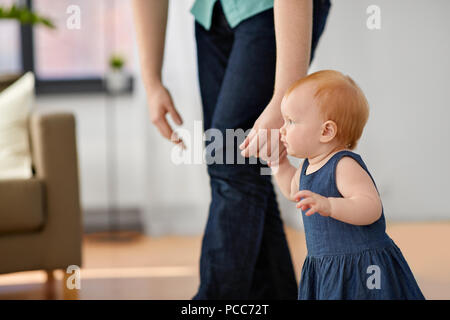 Baby Mädchen gehen mit Vaters Hilfe zu Hause Stockfoto