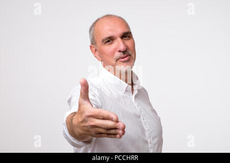 Sie sind herzlich Willkommen. Fröhliche reifer Mann im weißen Hemd Gestik Willkommen Zeichen und lächelnd Stockfoto