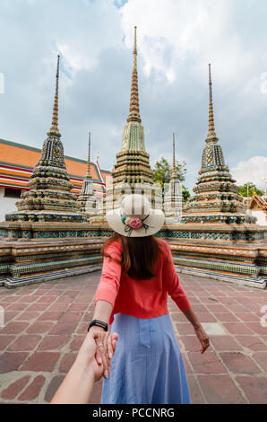 Porträt der schönen Asiatin führt Ihr Partner von Hand zu den berühmten Wat Pho. Wat Pho ist eine buddhistische Tempelanlage in Bangkok, Thailand Stockfoto