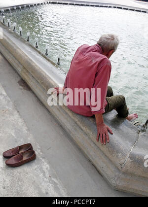 Alter Mann Gefühl heiß und unangenehm in die Hitzewelle versucht cool durch seine Füße in der kühlen Brunnen Wasser zu halten Stockfoto